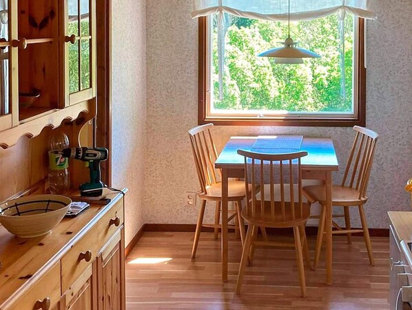 A dining area with a table and chairs, a window with a view of greenery, and wooden cabinets. - 6 Person Holiday Home in Brastad (Brastad)