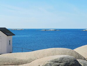 Une vue sur la côte, avec un bâtiment blanc et de gros rochers au premier plan.