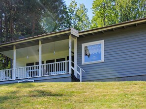 A single-story house with a covered porch, a small window with a decorative pattern, and a grassy yard. - 6 Person Holiday Home in Brastad (Brastad)