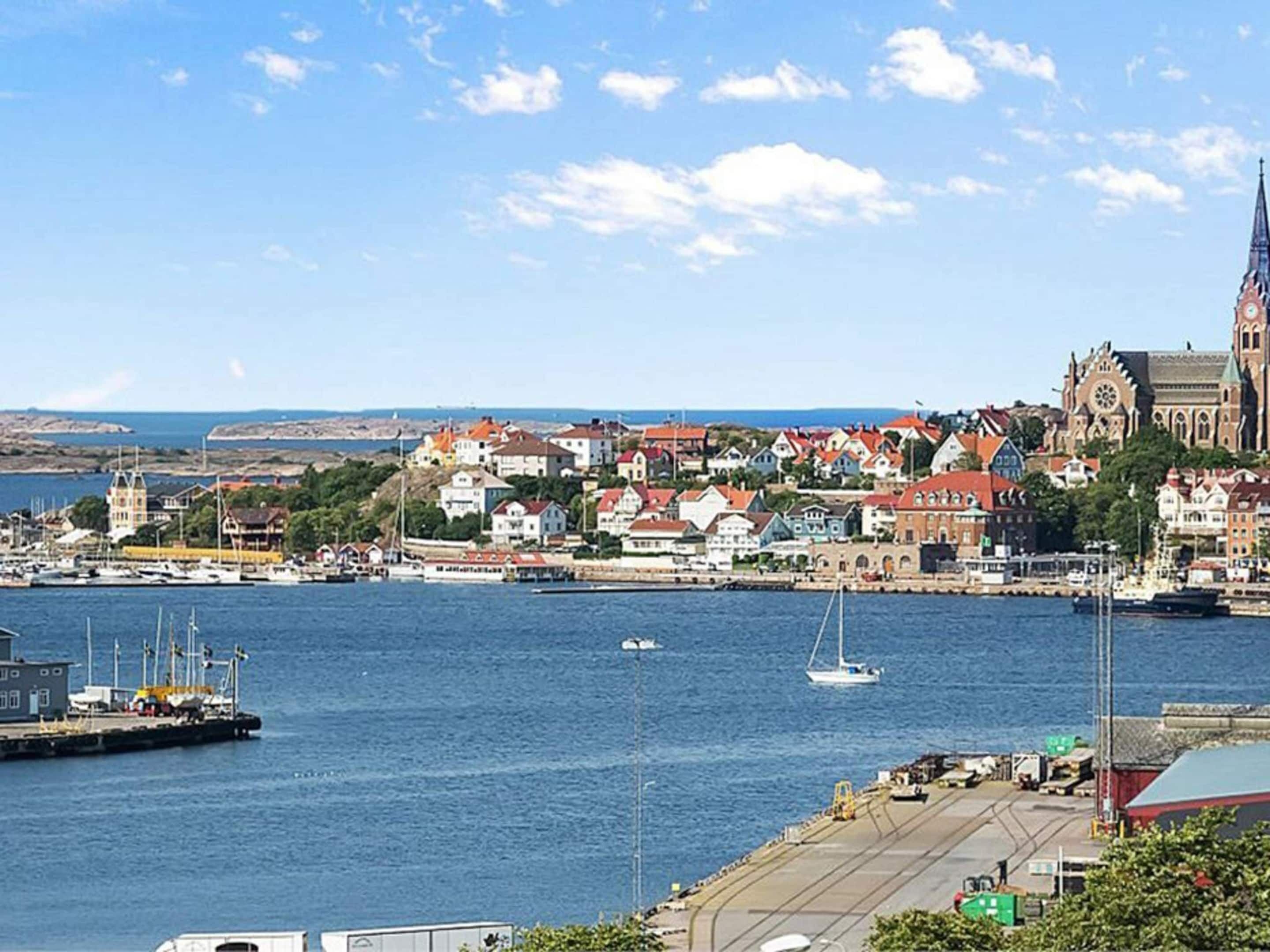 Una cittadina costiera con una chiesa imponente, un porto turistico con imbarcazioni e un mix di edifici residenziali e commerciali.