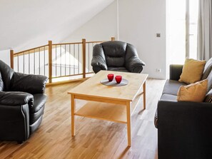 A modern living room with a wooden table, two black leather sofas, and a black leather armchair. - Holiday Home in Falkenberg (Glommen)