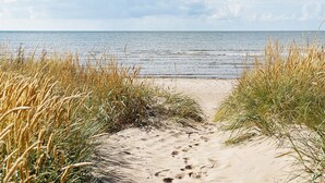 Een zandpad langs het strand dat naar de zee leidt, omringd door hoog gras.