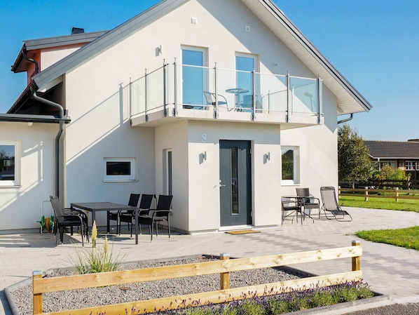 A modern two-story house with a balcony, outdoor seating, and a garden area.