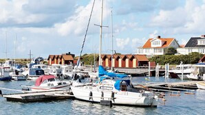 Uma marina com barcos atracados, uma fileira de casas com telhados vermelhos e um céu claro.
