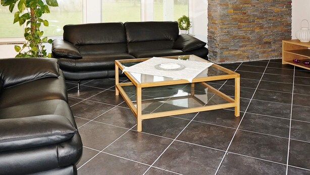 Uma sala de estar com um sofá de couro preto, uma mesa de centro de vidro e uma parede de pedra.