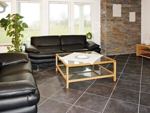 A living room with a black leather sofa, a glass-top coffee table, and a stone wall. - Holiday Home in Falkenberg (Glommen)