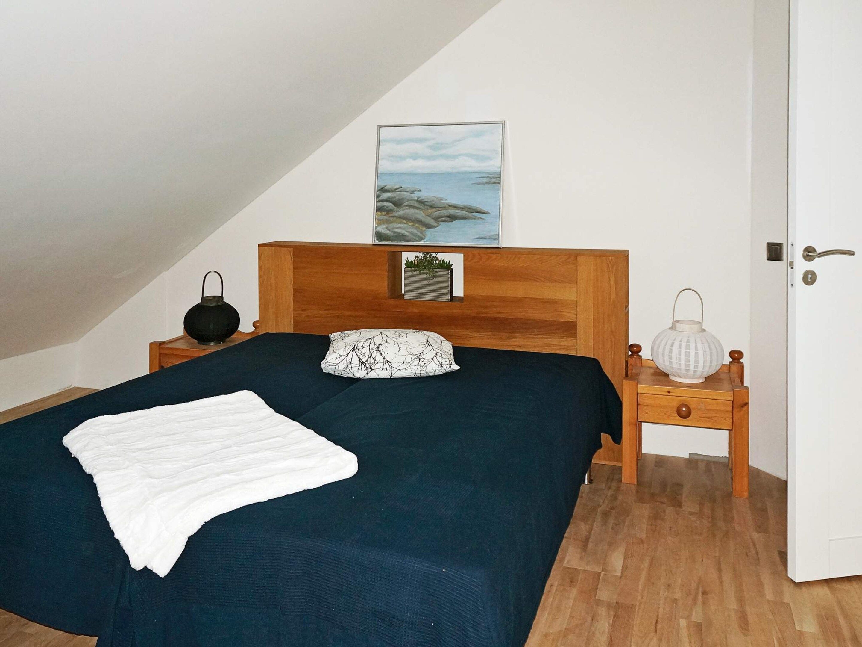 Un dormitorio con una cama, una mesita de noche, una lámpara, una puerta y un cuadro en la pared.
