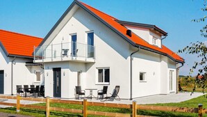 Een modern huis met twee verdiepingen, een rood dak, een balkon en een patio met tuinmeubilair.