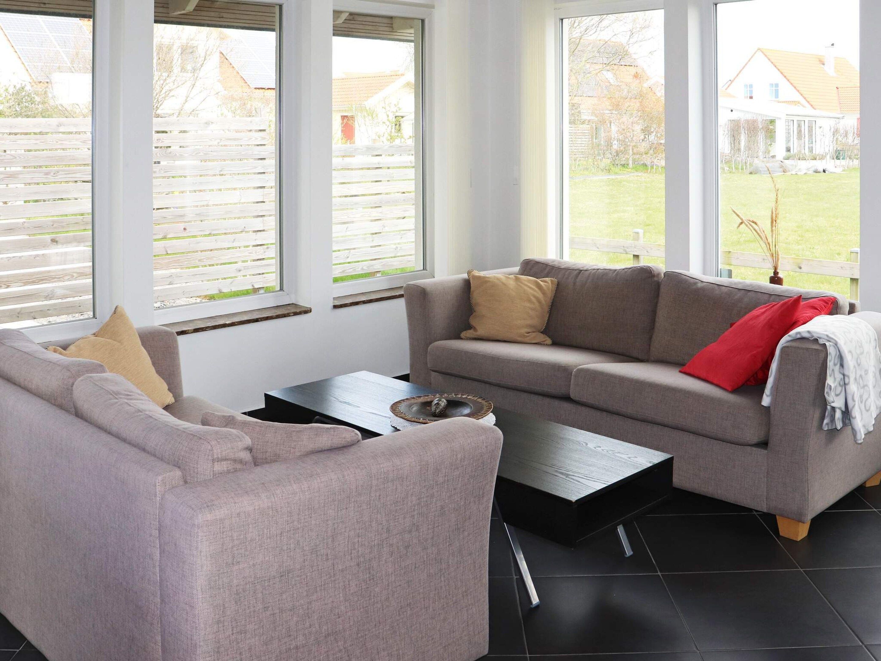 Una sala de estar moderna con un sofá gris, una mesa de centro y ventanas grandes con persianas.