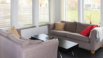 Una sala de estar moderna con un sofá gris, una mesa de centro y ventanas grandes con persianas.