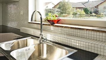 Una cocina con un lavamanos de acero inoxidable, una ventana con vistas a casas y un salpicadero de azulejos.