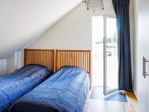 A bedroom with two beds, a wooden headboard, a door leading outside, and a small window. - Holiday Home in Falkenberg (Glommen)
