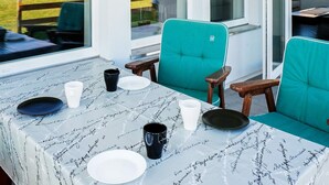 Een eethoek met een tafel voor vier personen, stoelen en uitzicht op een tuin en huizen.