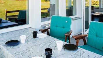 Un comedor con una mesa preparada para cuatro, sillas y vistas a un jardín y casas al exterior.