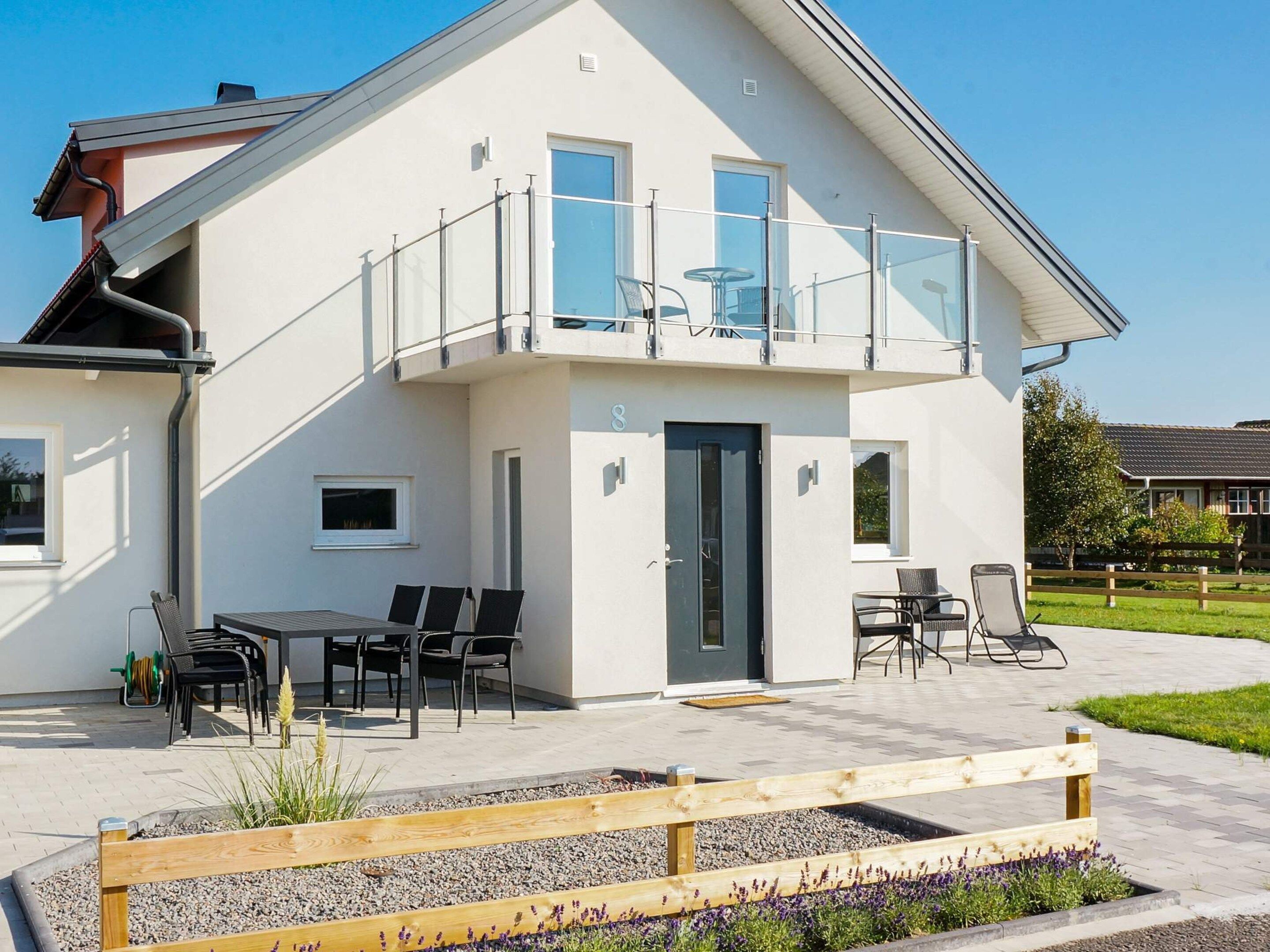 Une maison moderne à deux étages, dotée d’un balcon, d’un espace salon extérieur et d’un jardin.