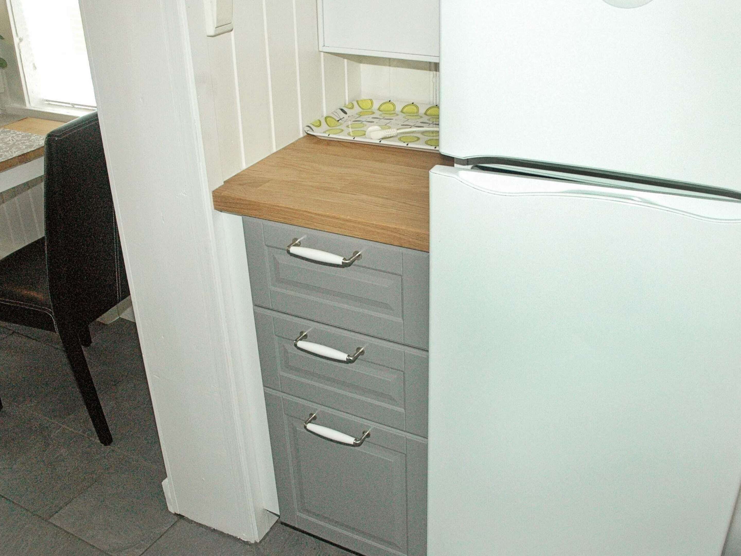A kitchen with a refrigerator, a wooden countertop, and a chair.