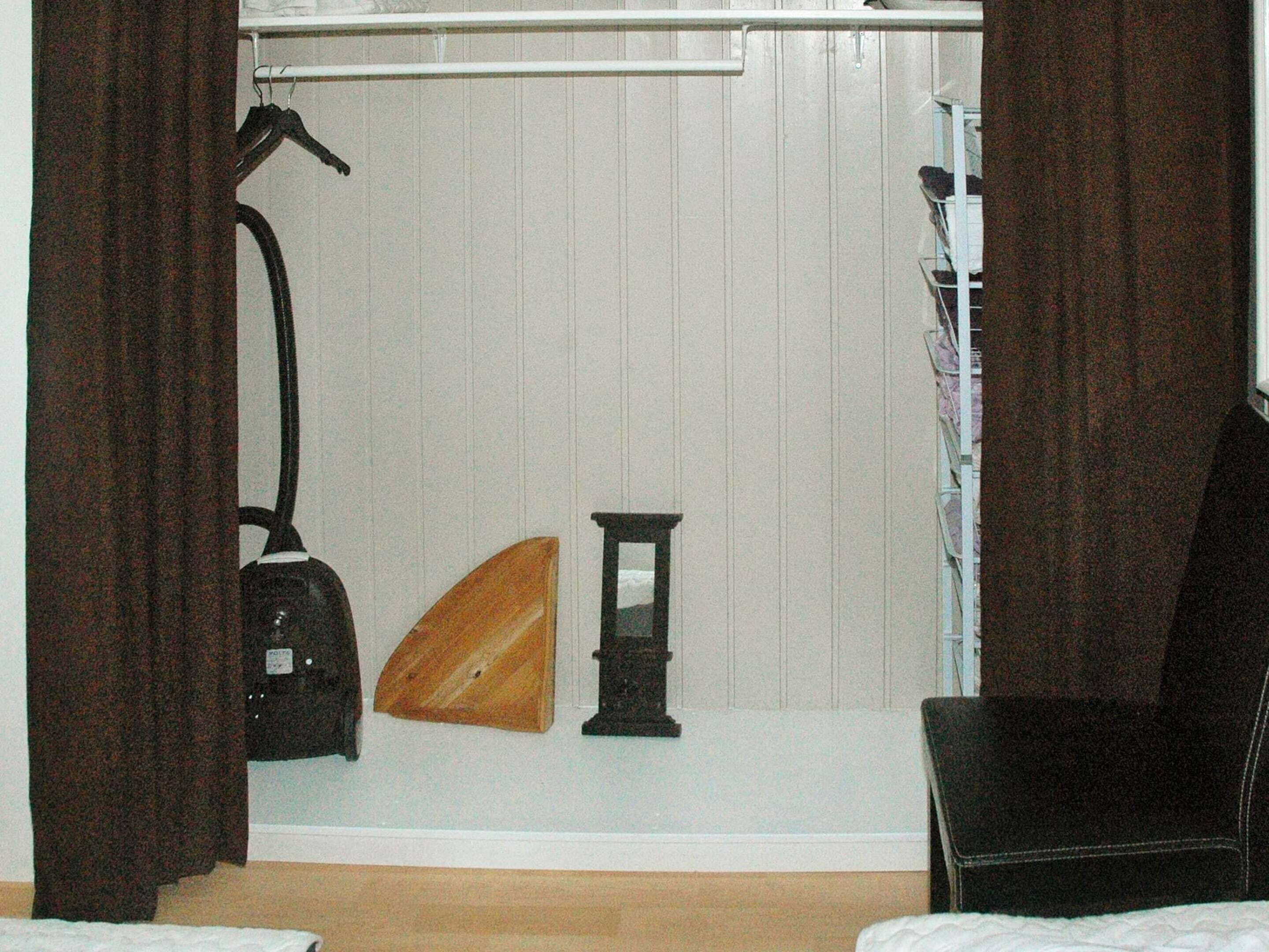 A room with a bed, a chair, a vacuum cleaner, and a small table.