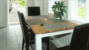 Een eethoek met een houten tafel, zwarte stoelen, een potplant en een televisie aan de muur.