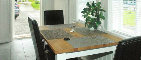 Un comedor con mesa de madera, sillas negras, planta en maceta y televisor en la pared.