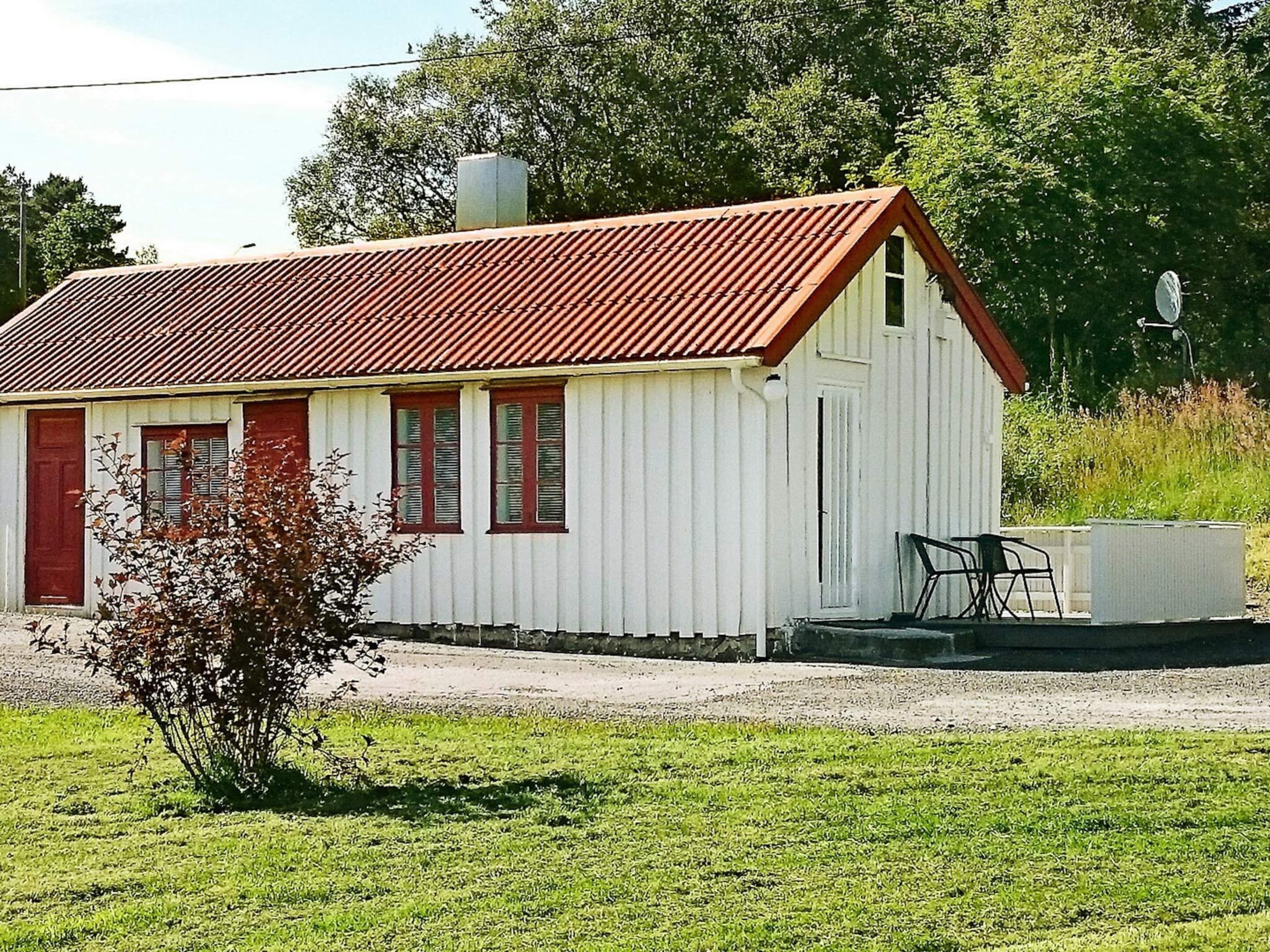 A small white building with a red roof, a door, and windows. There is a small tree in front of the building.