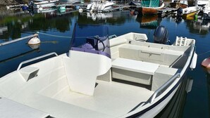Een kleine motorboot afgemeerd in een jachthaven, met een wit interieur, een motor aan de achterkant en een hut met een bank.