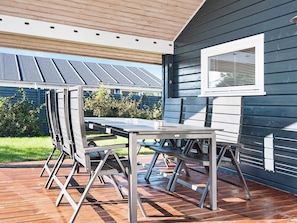 Une terrasse extérieure avec une table et des chaises, une terrasse en bois et une maison avec une fenêtre et un revêtement extérieur.