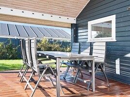 Un patio al aire libre con una mesa y sillas, una terraza de madera y una casa con ventana y revestimiento.
