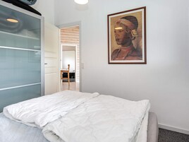 Un dormitorio con cama, un cuadro enmarcado en la pared y una puerta que conduce a otra habitación.