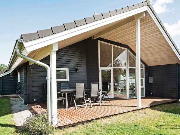 A modern house with a sloped roof, a wooden deck, and a glass door leading to an interior space.