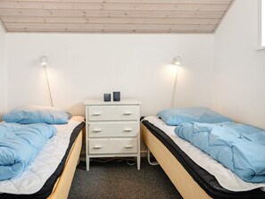 A small, single-room accommodation with two beds, a white dresser, and overhead lighting.