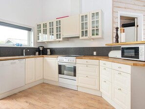 A kitchen with white cabinets, a black tiled backsplash, a wooden countertop, a built-in oven, and a microwave.