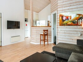 Una sala de estar moderna con un televisor de pantalla plana, un sofá gris y una mesa de comedor de madera con una silla.