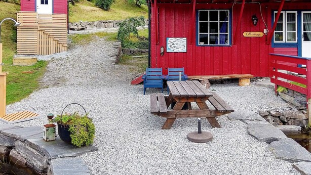 En rød træbygning med et skilt, der siger "Lillevagen", og et picnicbord med bænke.