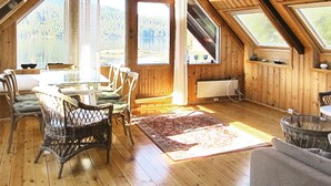 Et hyggeligt loftsværelse med trægulv, et spisebord med stole, et stort vindue der kigger ud over en sø, og et ovenlys.