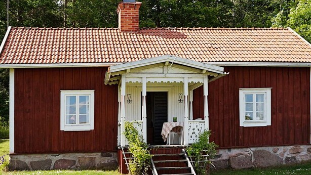 Ein rotes Holzhaus mit weißem Veranda, Schornstein und kleinem Garten.