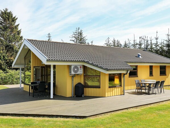 A yellow building with a covered patio, outdoor seating, and an air conditioning unit.