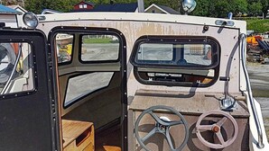 L'intérieur d'un bateau, avec un volant, un petit compartiment et une fenêtre.