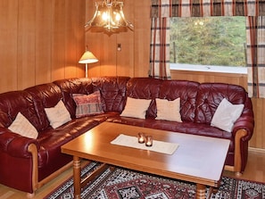 A leather sofa with cushions, a wooden coffee table, a lamp, and a window with curtains. - 8 Person Holiday Home in Vagland (Heim)
