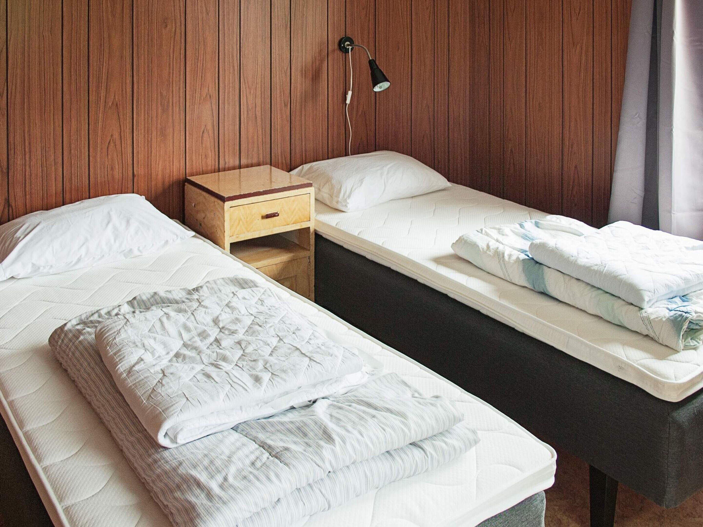 Une chambre avec deux lits simples, une table de chevet en bois, une lampe fixée au mur et une fenêtre avec des rideaux.