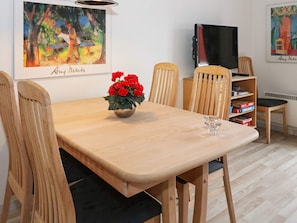 Een eethoek met een houten tafel, stoelen, een vaas rode bloemen, een glas en een boekenkast met boeken.