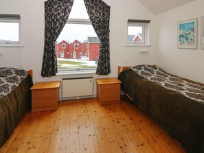 A dormitory room with two beds, a window with curtains, a radiator, and a small desk.