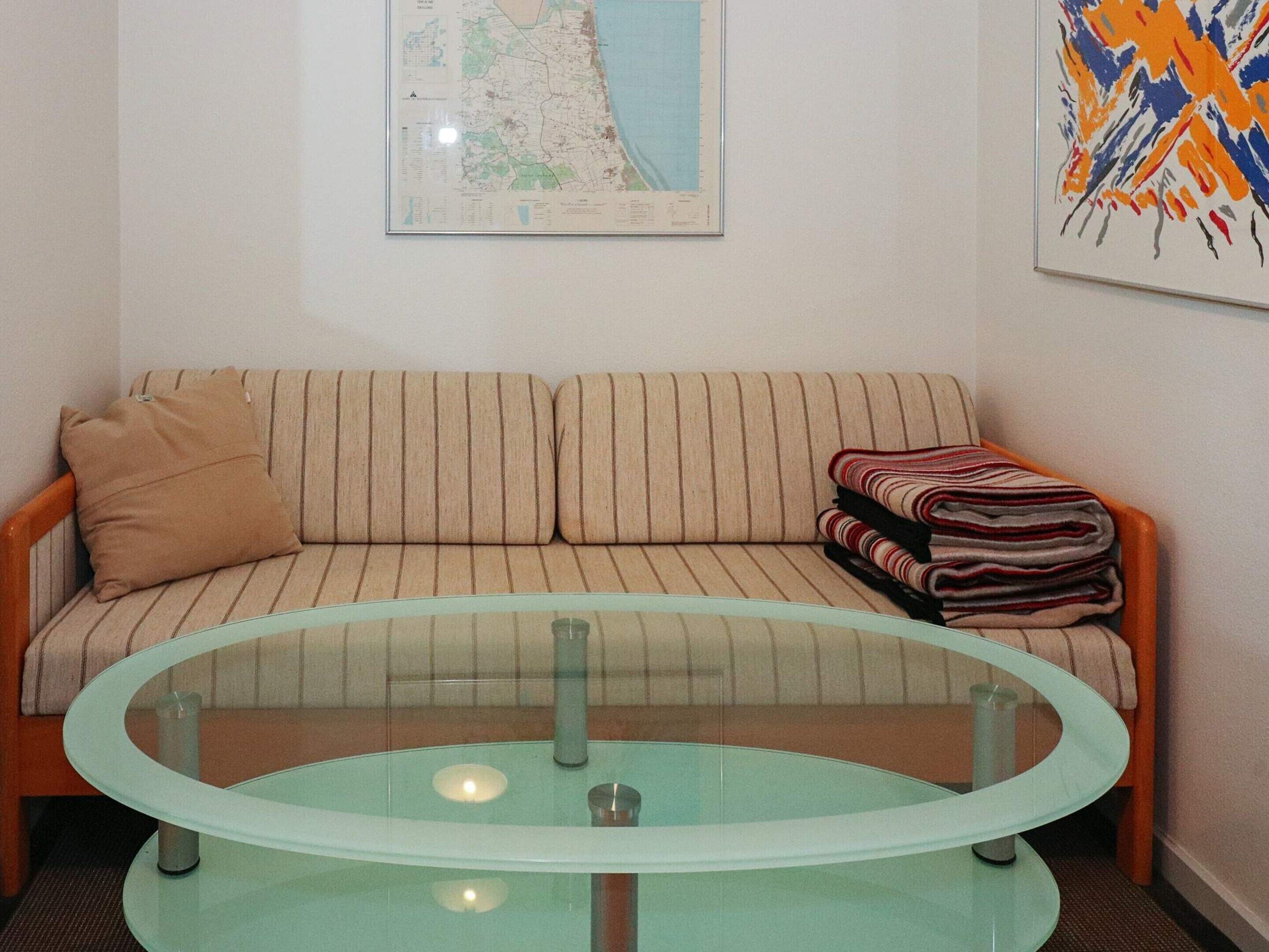 Une pièce avec un canapé à rayures, une table basse en verre, une carte accrochée au mur et un tableau abstrait aux couleurs vives.