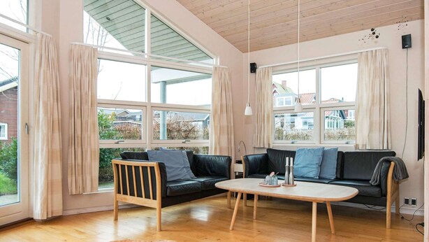 A modern living room with a wooden floor, two black leather sofas, a round coffee table, and a wicker ottoman. - 8 Person Holiday Home in Sjolund-by Traum (Sjølund)