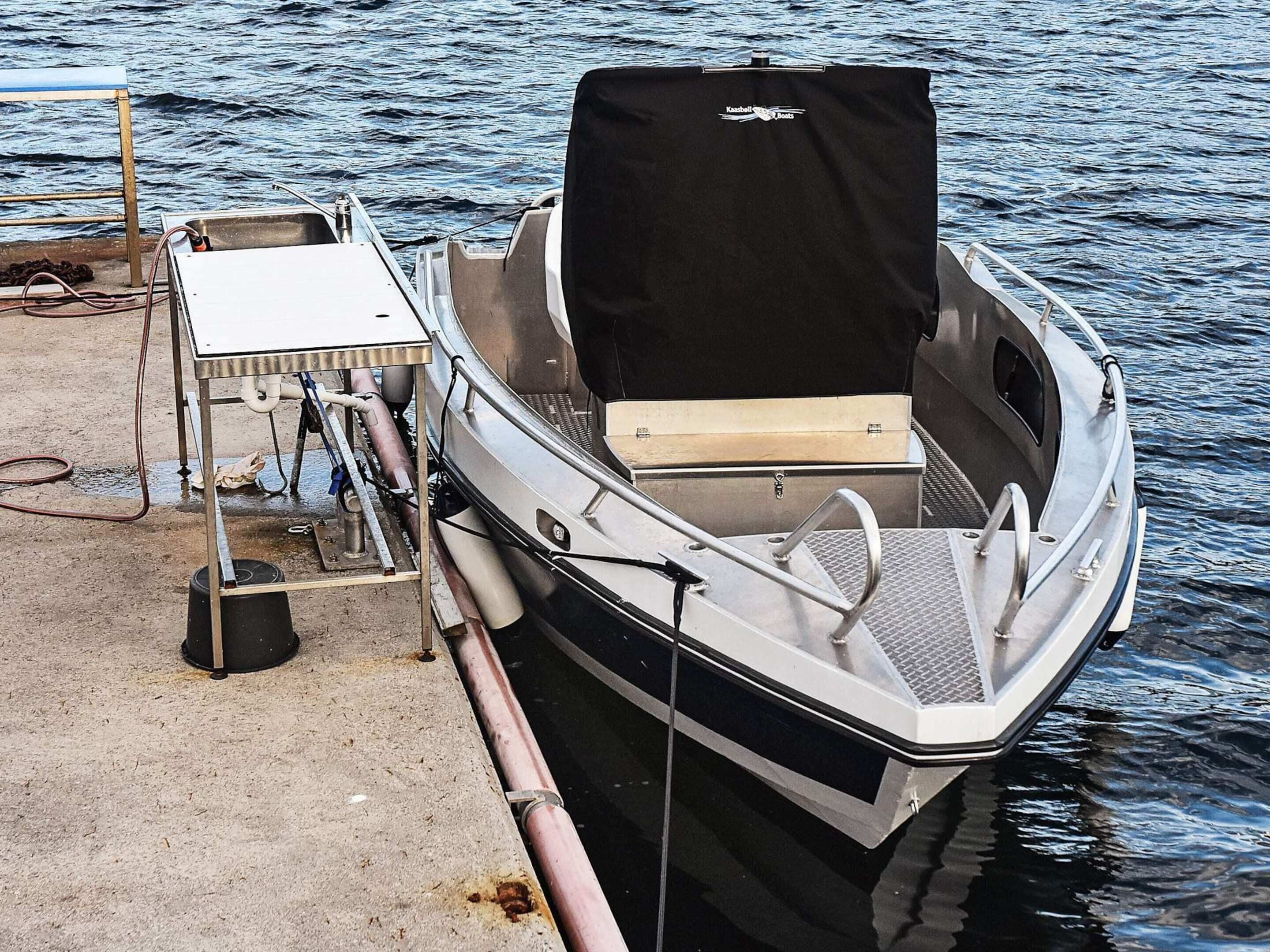 A small motorboat docked at a pier with a covered seating area and a metal table with a hose.