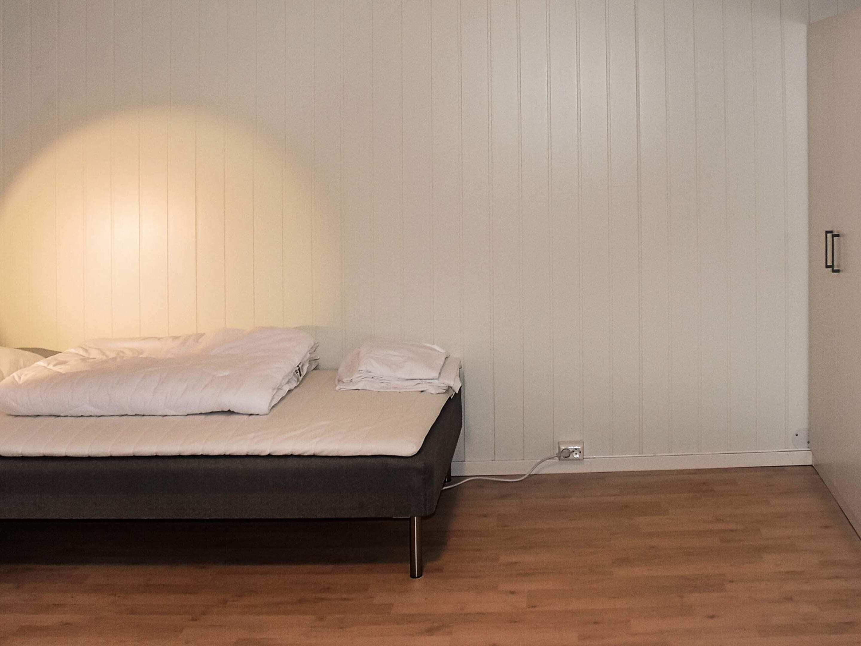 A neatly made bed with white linens, a wooden floor, and a white wall with a vertical panel design.