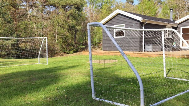 Ein durch einen Zaun abgegrenztes Fußballtor mit einem Haus im Hintergrund.