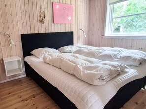Ein Bett mit weißer Bettwäsche in einem Zimmer mit Holzwänden und einem Fenster.
