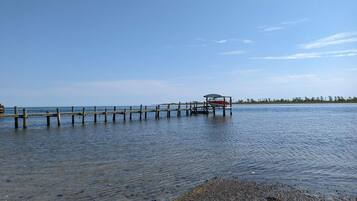 A wooden pier extending into calm water, a small boat docked at the end, and a distant shoreline with trees.