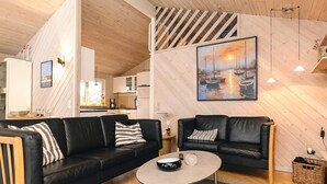 A modern living room with two black leather sofas, a round coffee table, and a painting of boats on the wall.