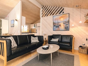 A modern living room with two black leather sofas, a round coffee table, and a painting of boats on the wall.